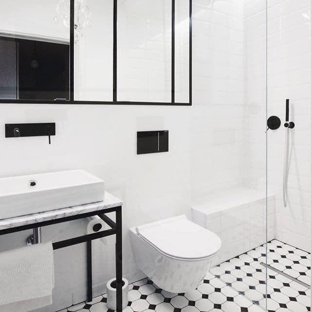 Carrelage uni blanc 10x10 cm dans une salle de bain moderne avec murs blancs, sol à motifs géométriques noirs et blancs, sanitaire blanc et accents noirs