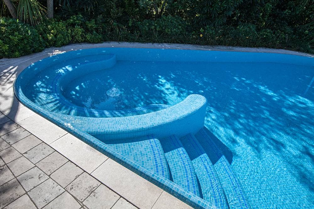 Carrelage uni bleu clair 30x30 cm sur les bords de piscine extérieure, contrastant avec dallage beige, entouré de verdure