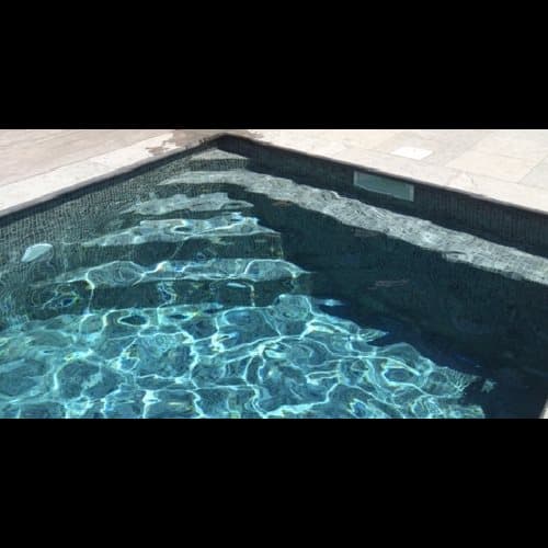 Carrelage uni gris 30x30 cm en bordure de piscine, contrastant avec leau claire et le revêtement intérieur bleu