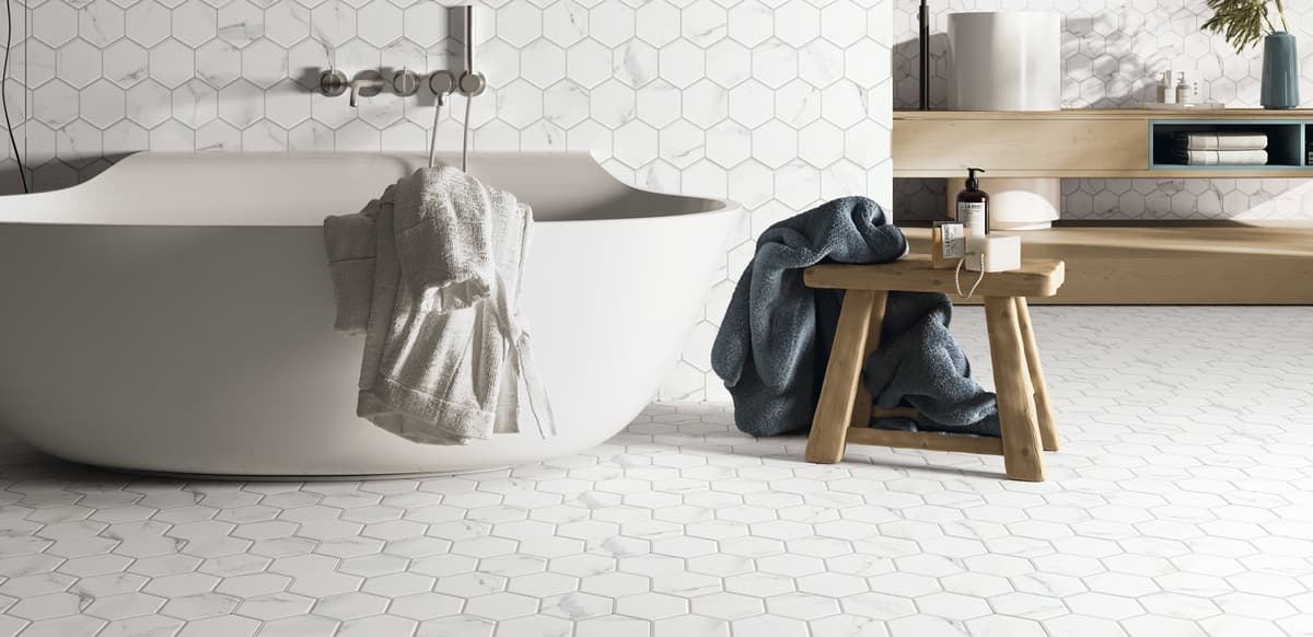 Carrelage blanc relief hexagonal dans une salle de bain épurée avec mobilier en bois clair et serviettes bleues et grises sur élégante baignoire ovale