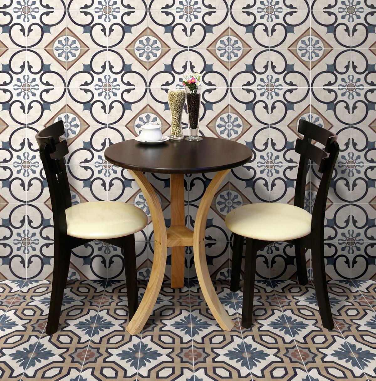 Carreau de ciment multicouleur avec motifs géométriques et floraux 20x20 cm dans un coin repas aux murs beige et blanc avec table ronde et deux chaises noires