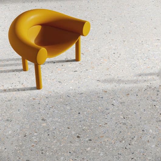 Carrelage blanc Terrazzo 60x60 cm avec nuances de gris et éclats colorés sur une chaise design jaune dans un environnement lumineux