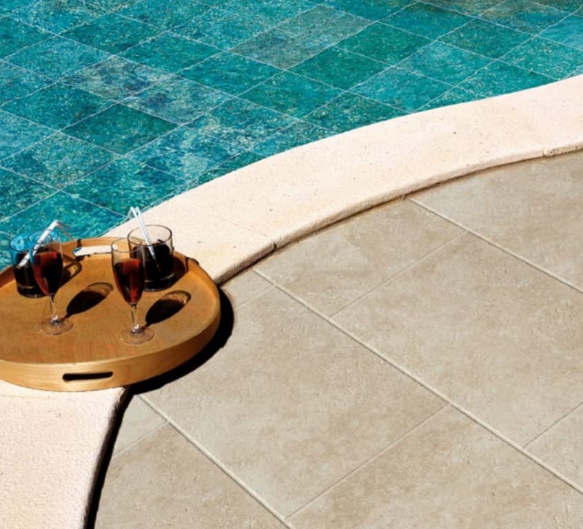 Carrelage aspect pierre couleur beige uni 40x60 cm près dune piscine aux eaux bleues sur terrasse extérieure avec verres de vin