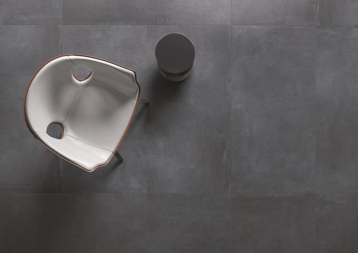 Carrelage effet ciment noir uni 60x60 cm dans un intérieur avec fauteuil design gris et table ronde noire épurée