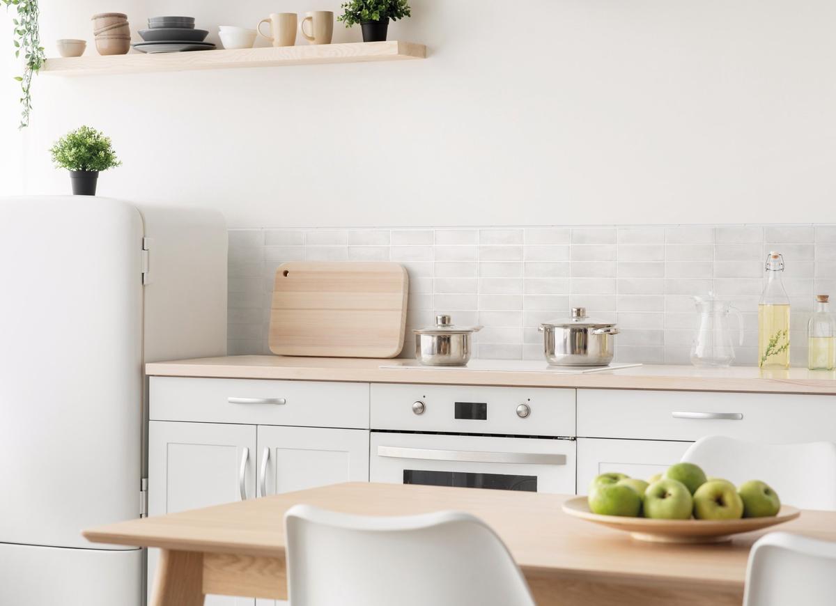 Carrelage Zellige blanc 5X15 dans une cuisine moderne aux murs blancs et meubles en bois clair, plans de travail et étagère en bois, avec réfrigérateur et vaisselle