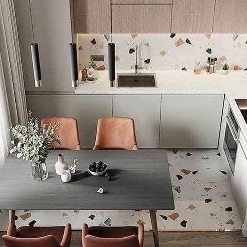 Carrelage Terrazzo nuances terracotta et beige dans cuisine moderne sur sol et crédence, associé à meubles gris et chaises en cuir caramel
