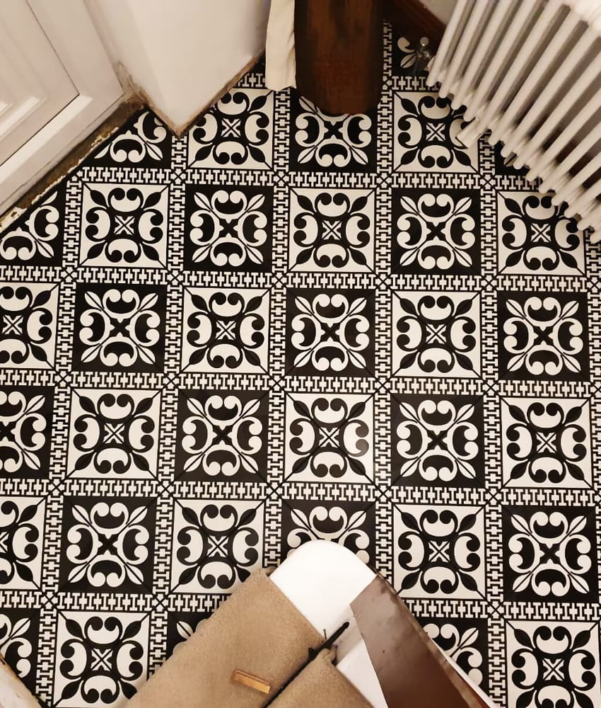 Carreau de ciment noir avec motifs blancs élégants 20x20 cm sur un sol dans une pièce aux murs blancs avec plinthes et radiateur