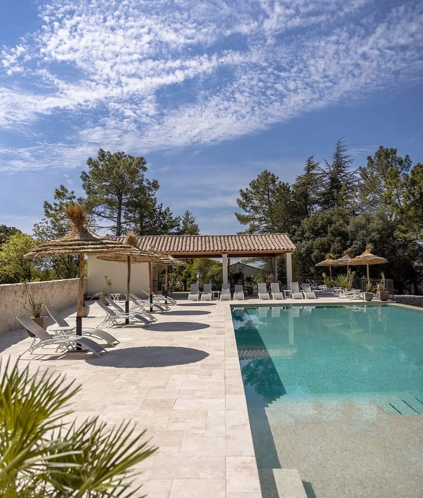 Carrelage en pierre beige uni sur une terrasse extérieure autour d’une piscine avec mobilier blanc et parasols naturels, nuances