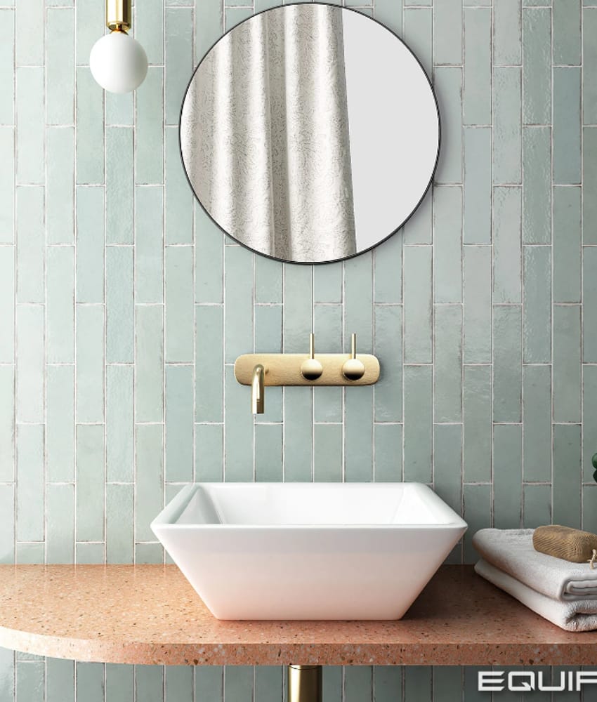 Carrelage Zellige vert clair uni sur mur de salle de bain épurée avec lavabo blanc sur plan de travail terrazzo beige et accesso