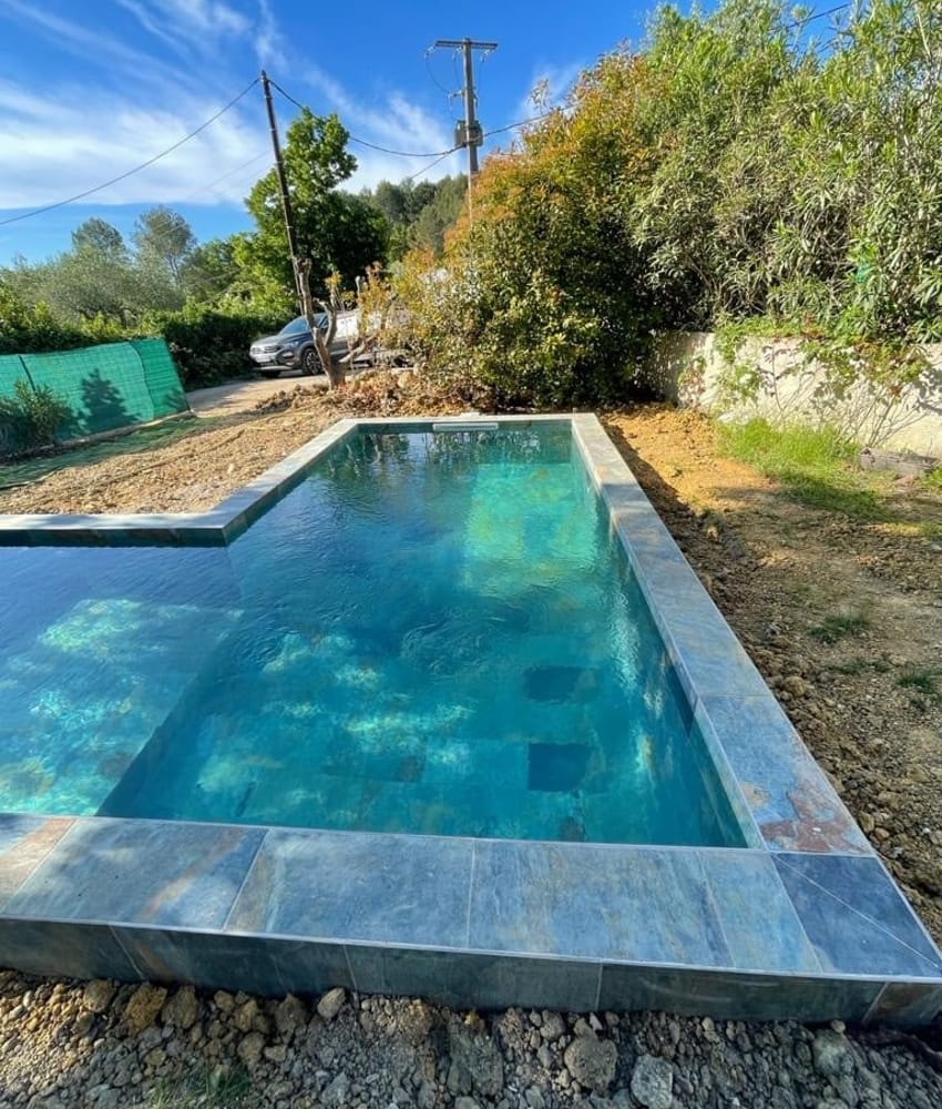 Carrelage pierre multicouleur nuances de gris et bleu 30x60 cm sur bord de piscine extérieure entourée de végétation