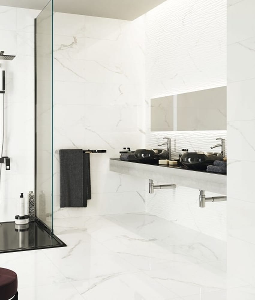 Carrelage blanc marbré sans motifs dans une salle de bain moderne, sur le sol et les murs, avec douche et lavabos noirs