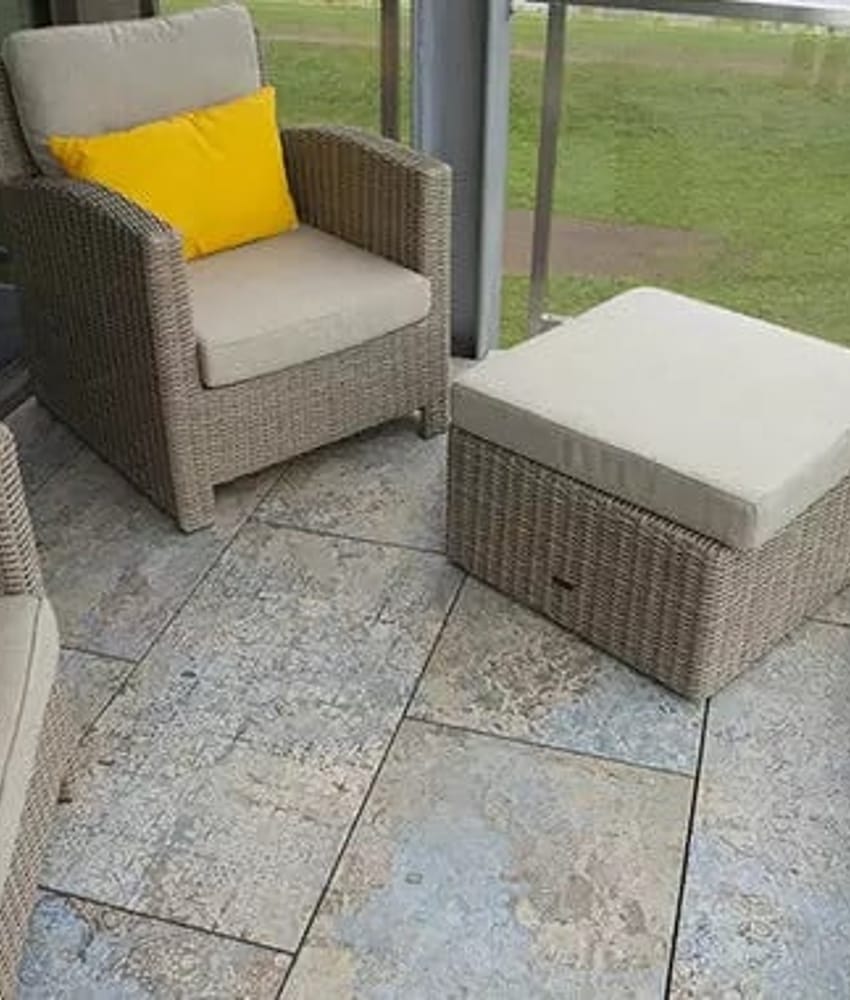 Carrelage effet tissu beige nuancé de bleu sans motifs 50x100 cm dans une véranda sur fond de pelouse verte avec mobilier rotin 