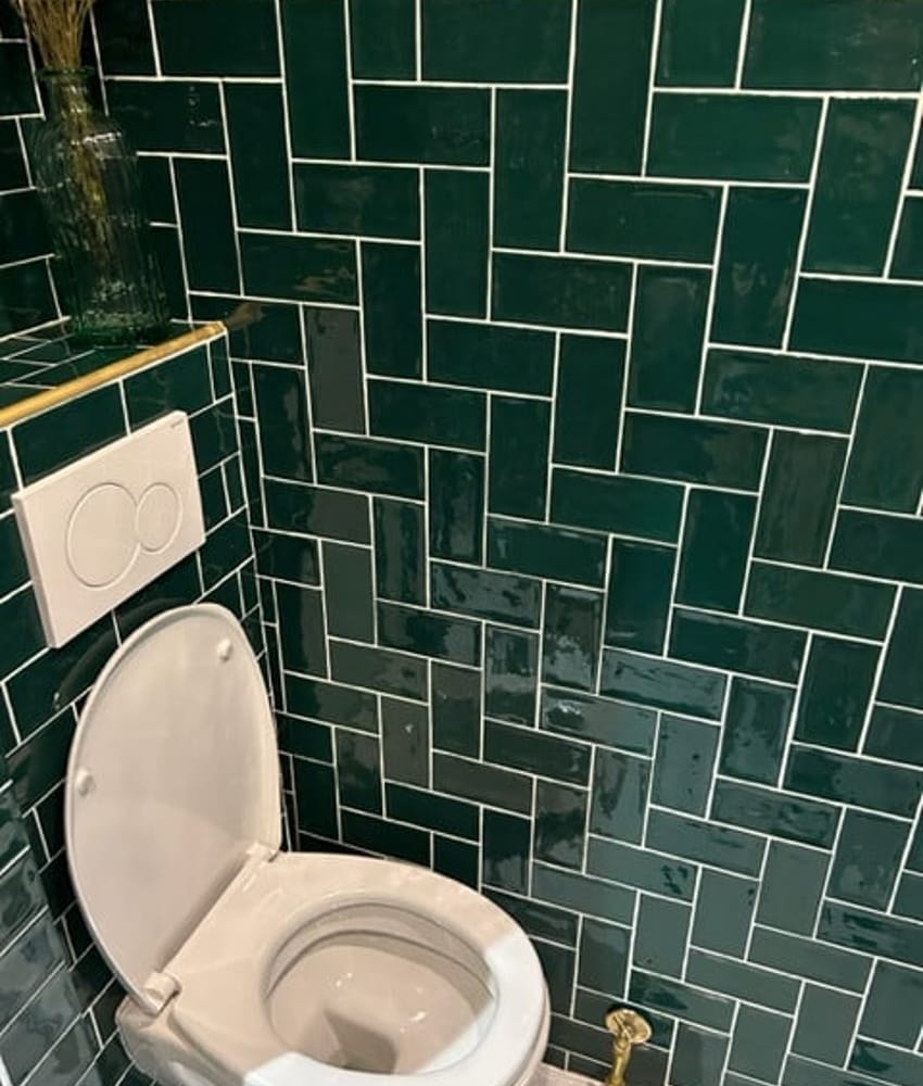Carrelage uni vert 7,5x15 cm sur les murs de la salle de bain, combiné avec des sanitaires blancs et des éléments dorés