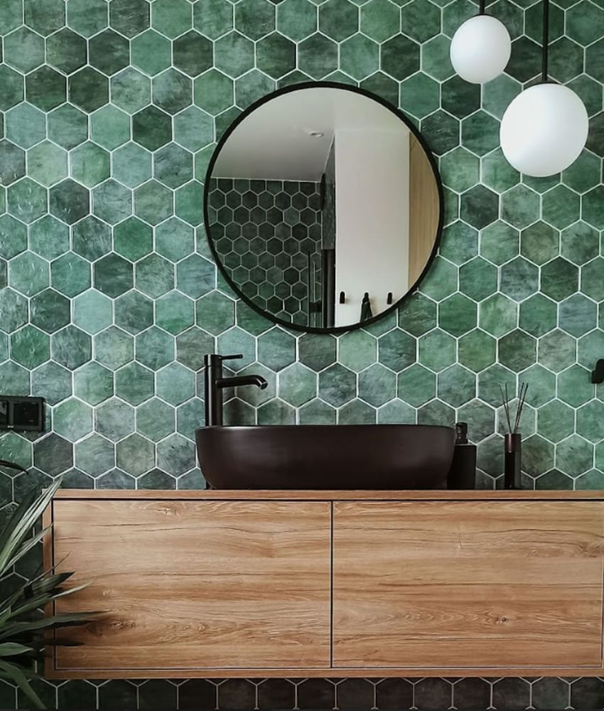 Zellige vert émeraude brillant sur mur salle de bains avec meuble bois marron, vasque noire, miroir rond, luminaires suspendus b