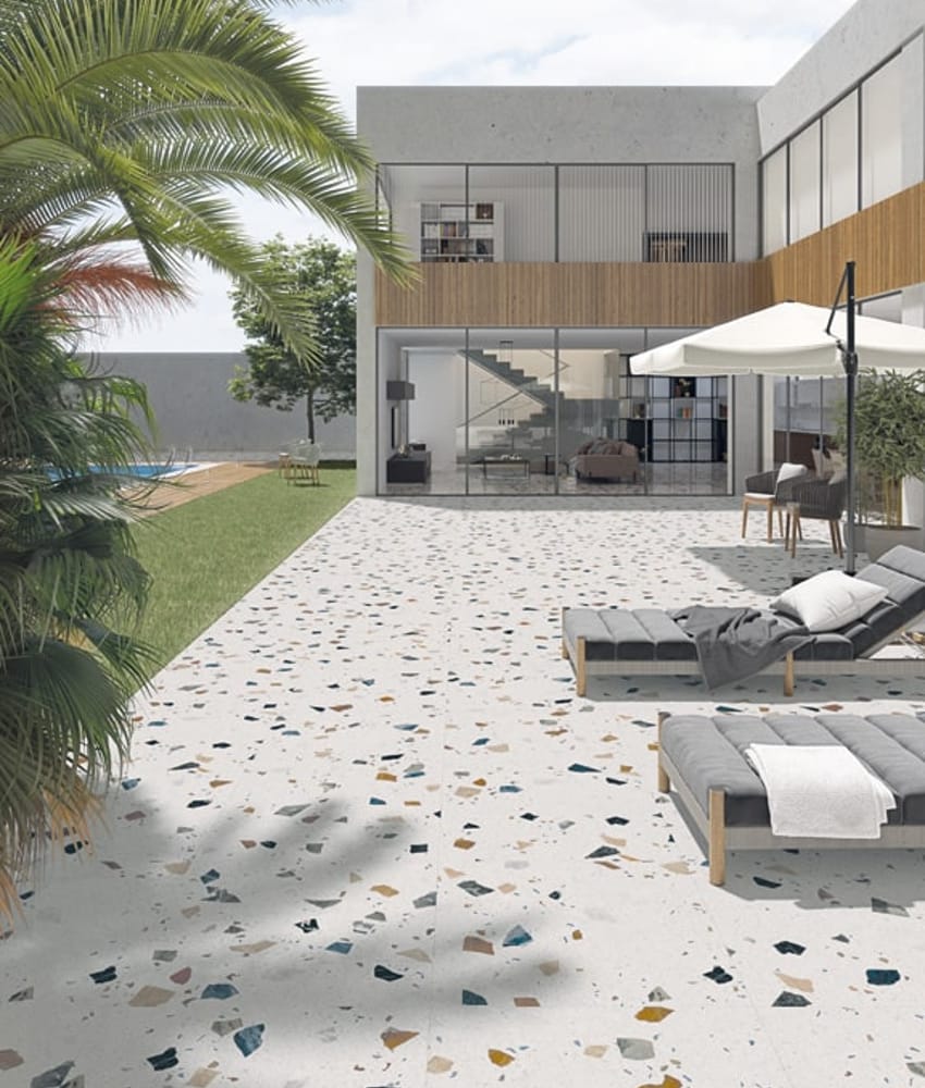 Carrelage Terrazzo blanc parsemé de motifs colorés 60x60 cm dans une cour extérieure tons neutres avec mobilier de jardin et vég