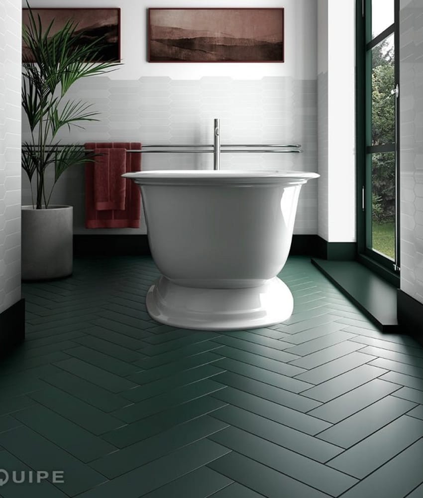 Carrelage uni vert dans une salle de bain avec mur blanc, baignoire centrale et accessoires rouges, vue sur jardin