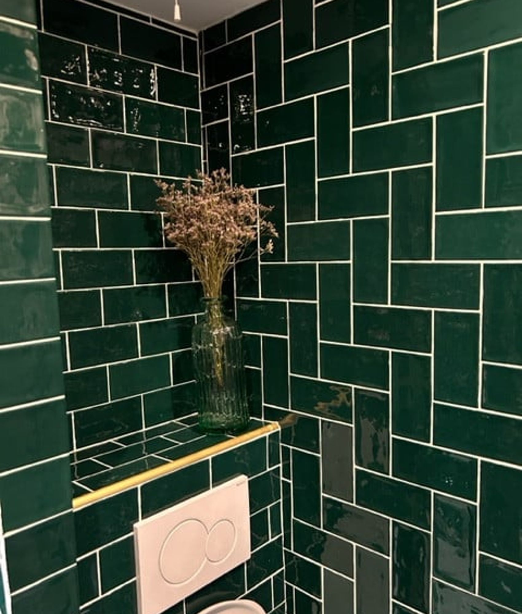 Carrelage uni vert émeraude brillant 7,5x15 cm sur un mur de salle de bain blanche avec vase et fleurs séchées