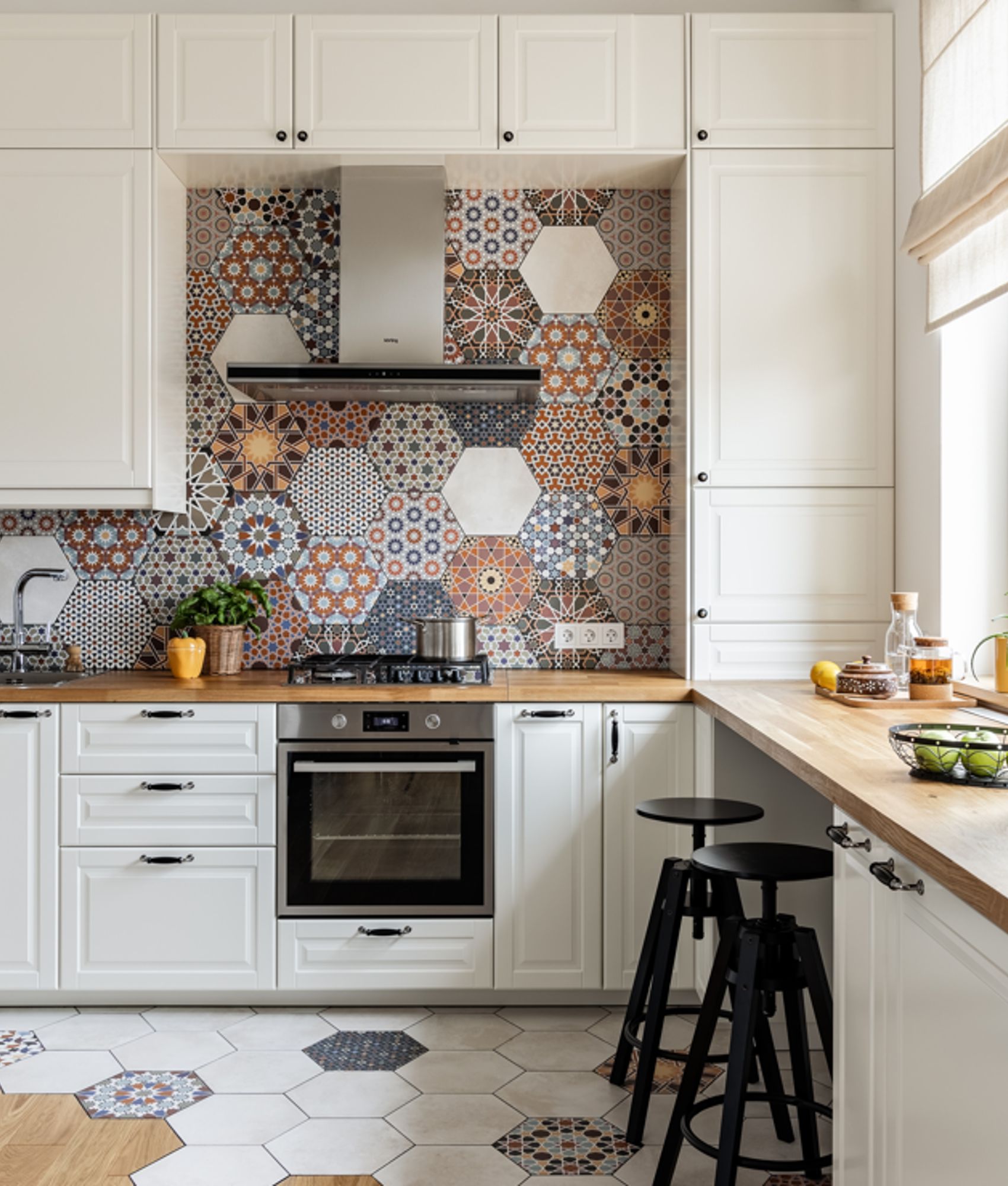 Carreau de ciment coloré terracotta motifs variés 30x30 cm dans une cuisine blanche avec plans en bois et tabourets noirs